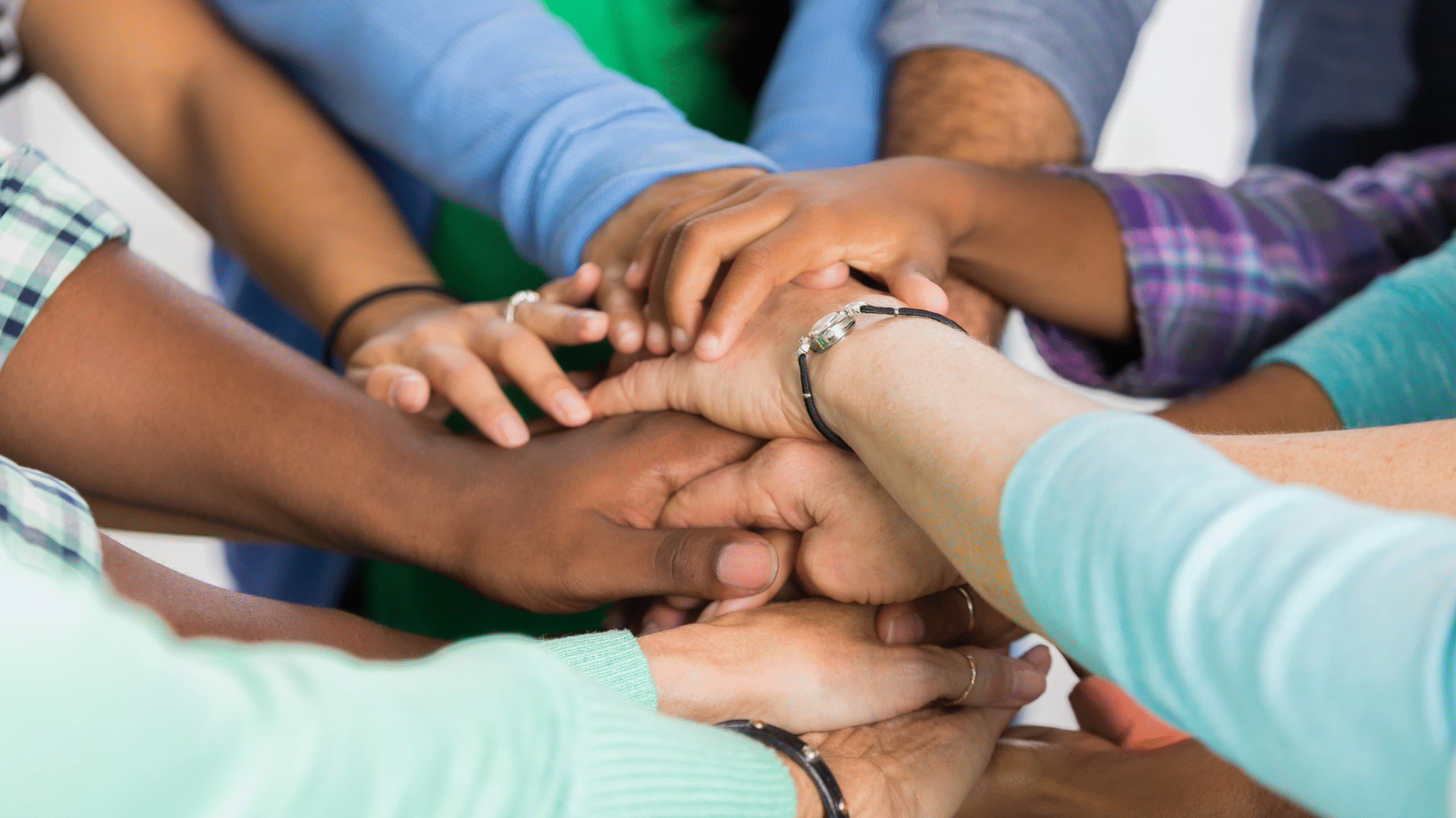 A community with their hands piled on top of each showing unity.