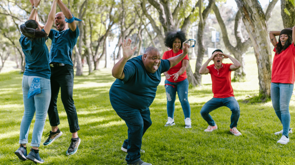 A man in a park waving his hands in a fun way in a community group with happy volunteers behind him.