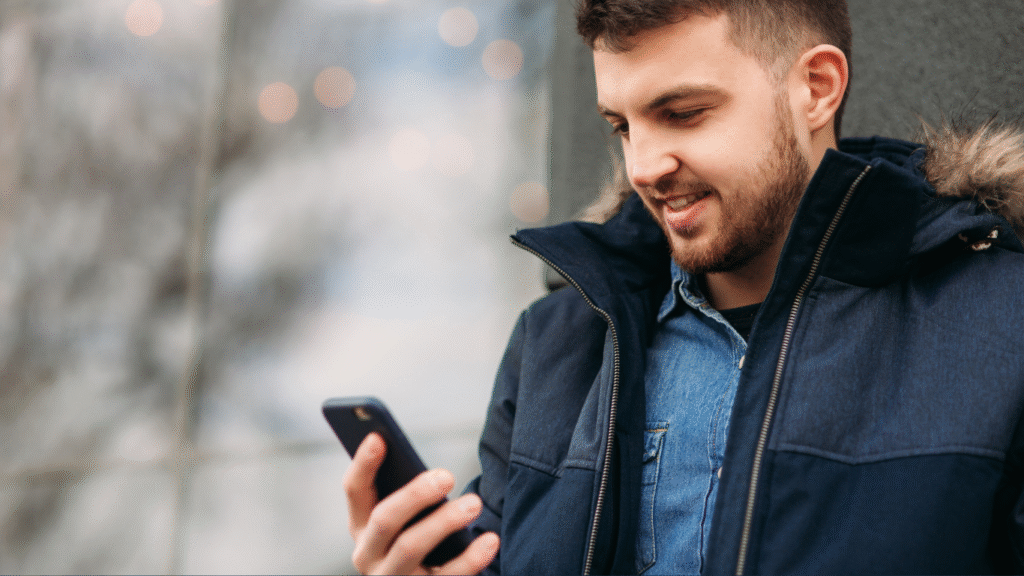 A man outside in a warm jacket on a cold day looking at his mobile phone and smiling.