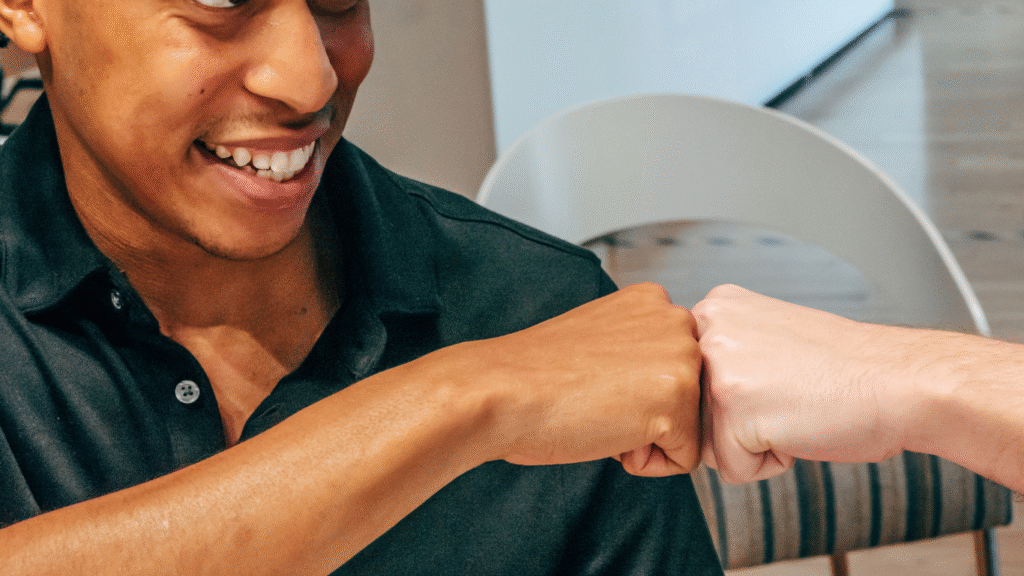 A man smiling fist bumping someone else in support of an achievement.