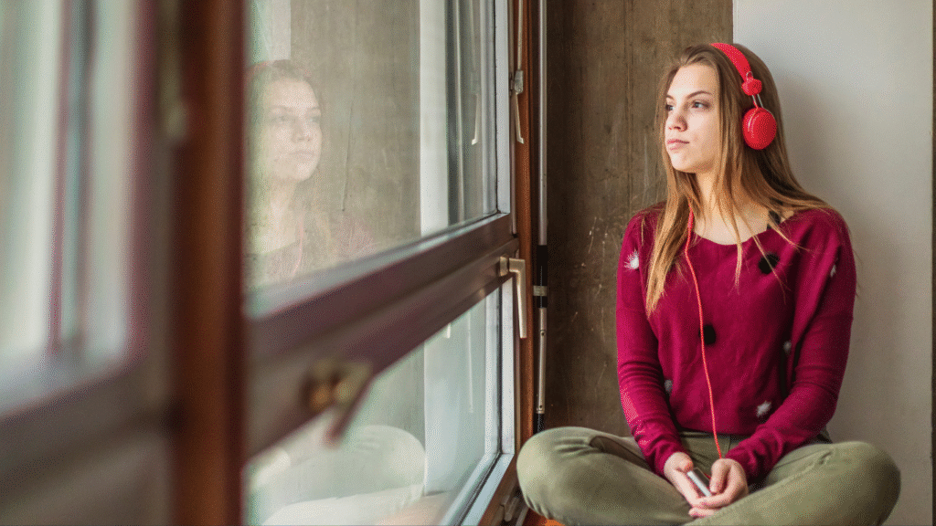 A young girl looking out the window thinking about life with headphones on.