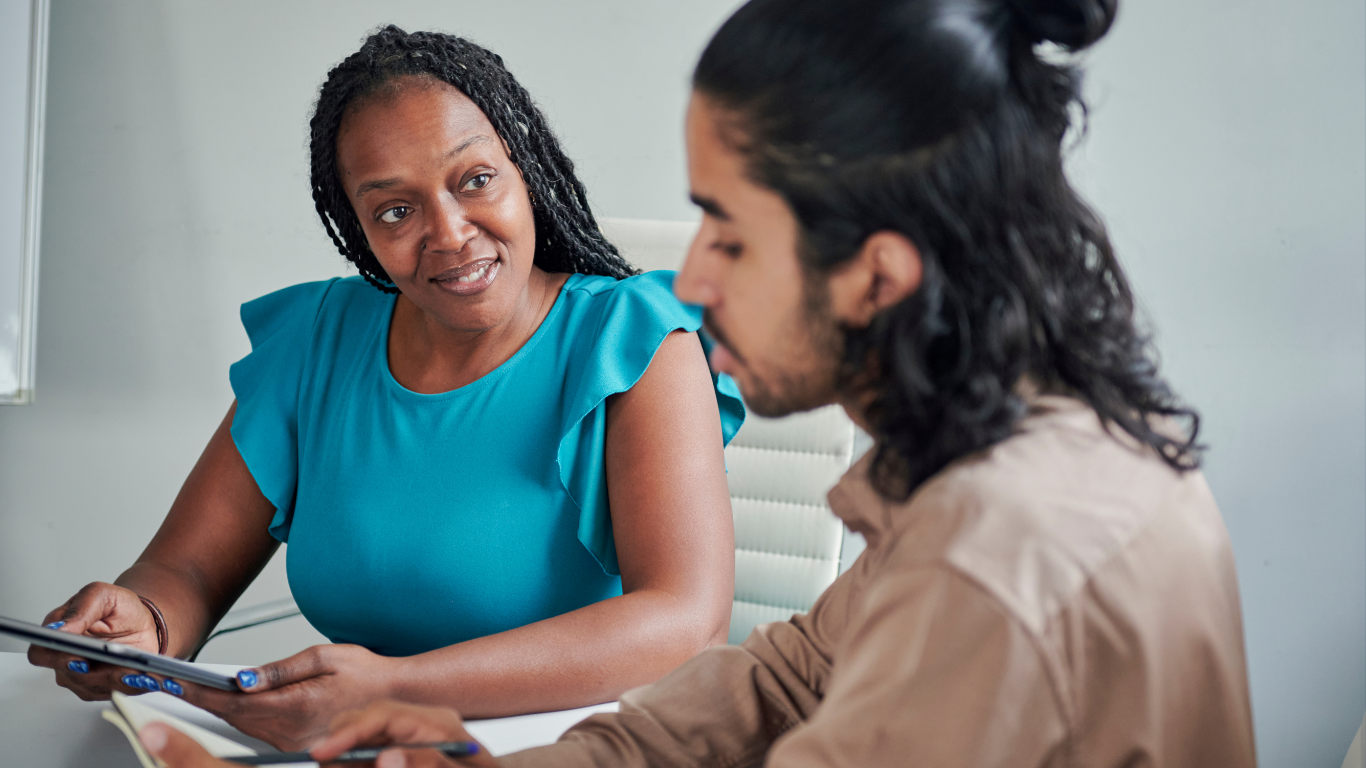 A woman supporting a younger male in the workplace with training.